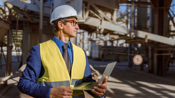 Male Worker With Laptop Standing Outdoors At Factory - Quero montar uma empresa